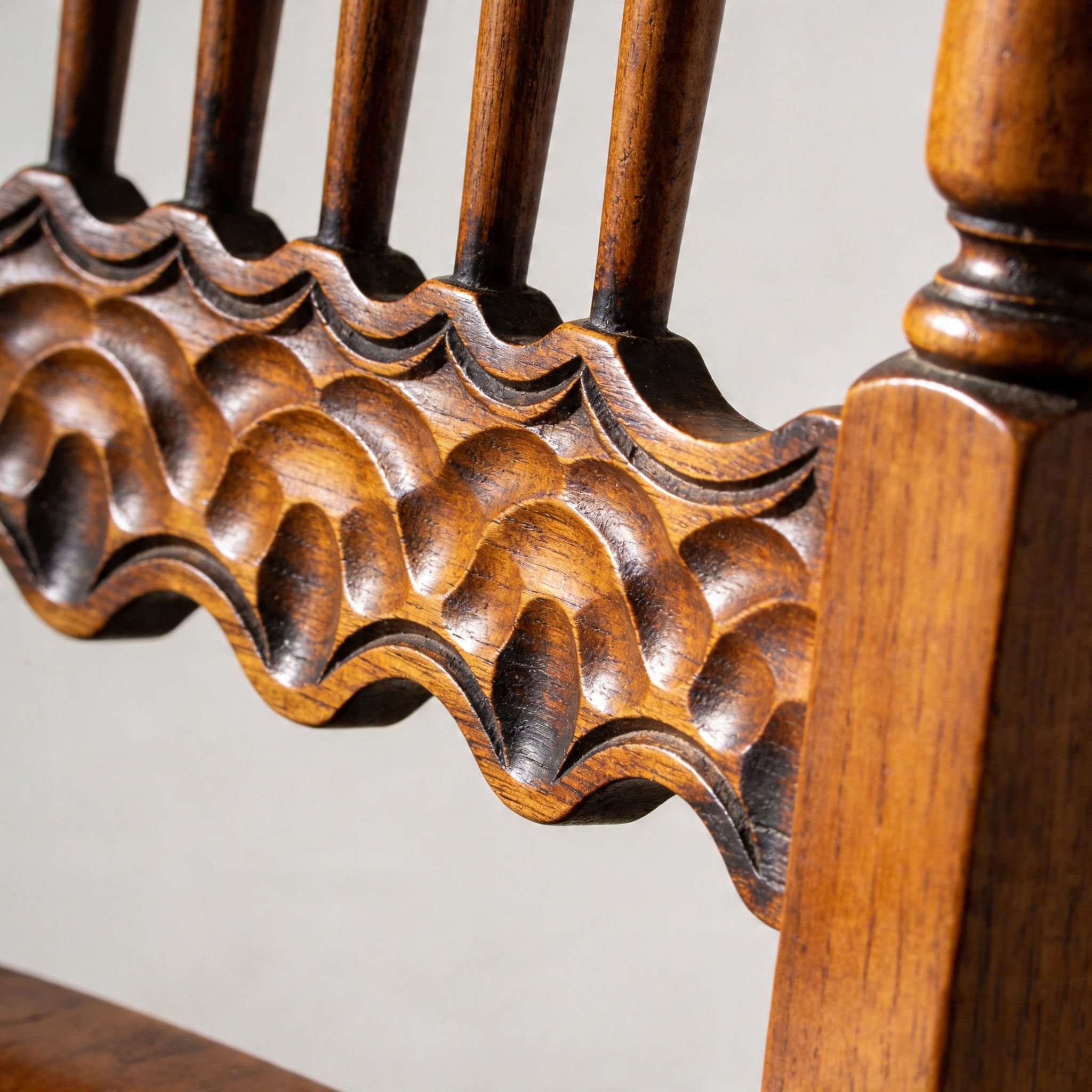 Close-up of the hand-shaped scalloped apron on a spindle-back chair seat-rail in honey-waxed mango, raking light showing spokeshave facets.