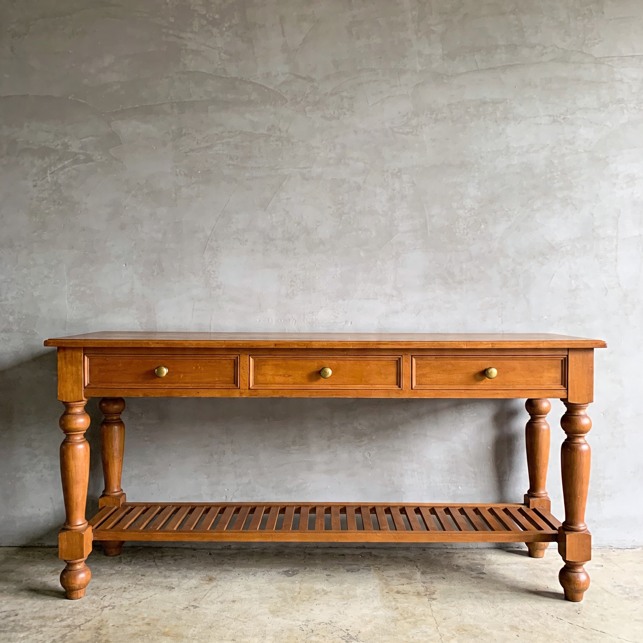 A long console table in reclaimed haveli-teak wood with four hand-forged iron square legs against a lime-washed plaster wall.